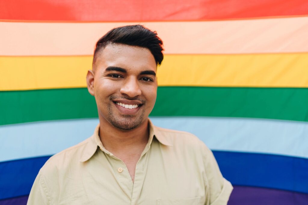 Portrait of a young gay man with rainbow flag on background